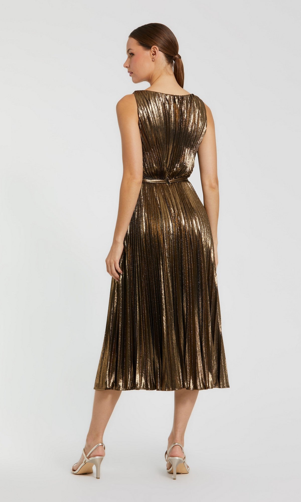A woman models the Mac Duggal 27611 sleeveless midi party dress, facing away from the camera against a simple backdrop. The shimmering gold metallic pleated design of the dress pairs perfectly with her white heeled sandals, creating an elegant yet contemporary look.